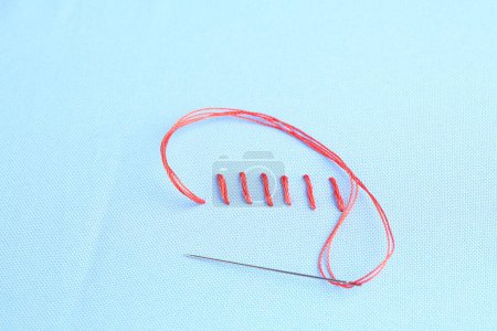 Téléchargez les photos : Aiguille à coudre avec fil et points de suture sur tissu bleu clair, vue ci-dessus - en image libre de droit