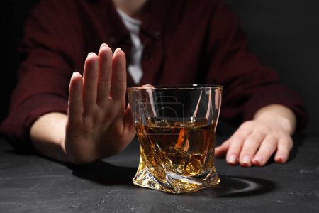 Alcohol addiction. Woman refusing glass of whiskey at dark textured table, closeup