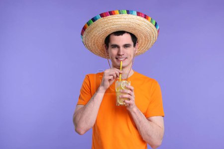 Joven en sombrero mexicano con cóctel sobre fondo violeta