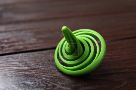 One green spinning top on wooden table, closeup. Space for text