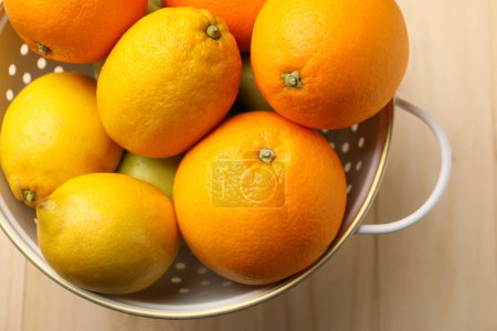 Colander with fresh citrus fruits on wooden table, top view