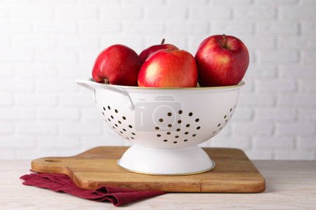 Fresh apples in colander on white wooden table