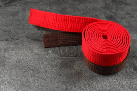 Cinturones de karate rojos y marrones sobre fondo texturizado gris, espacio para texto
