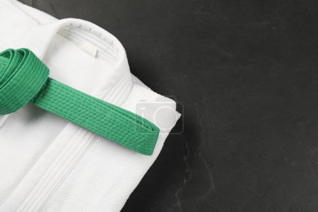 Green karate belt and white kimono on gray background, top view. Space for text