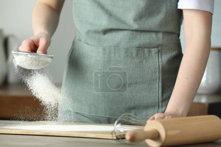 Femme tamisant la farine à table dans la cuisine, gros plan