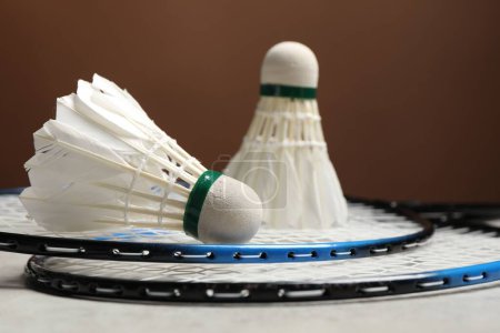 Photo for Feather badminton shuttlecocks and rackets on gray table against brown background, closeup - Royalty Free Image