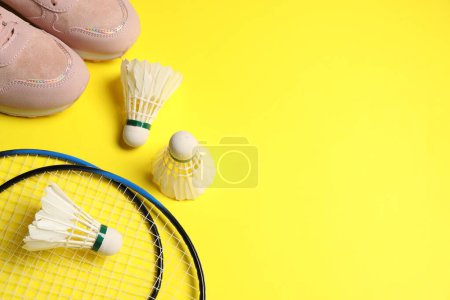 Photo for Feather badminton shuttlecocks, rackets and sneakers on yellow background, above view. Space for text - Royalty Free Image