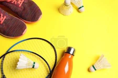Photo for Feather badminton shuttlecocks, rackets, sneakers and bottle on yellow background, above view. Space for text - Royalty Free Image