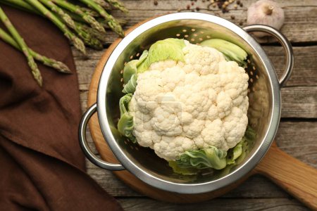 Metal colander with cauliflower, fennel and asparagus on wooden table, flat lay