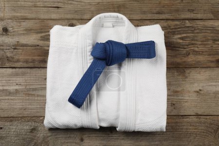 Blue karate belt and white kimono on wooden background, top view
