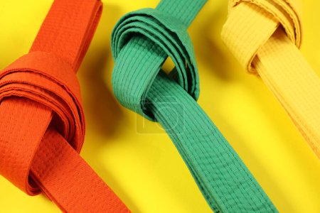 Colorful karate belts on yellow background, closeup