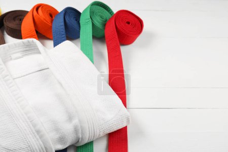 Colorful karate belts and white kimono on wooden background, closeup. Space for text