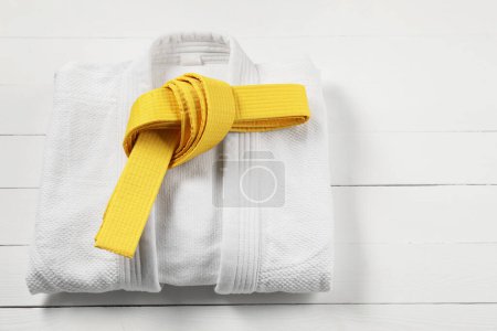 Yellow karate belt and white kimono on wooden background, space for text
