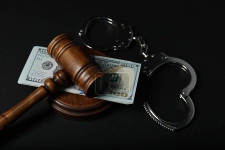 Law gavel, dollars and handcuffs on dark table