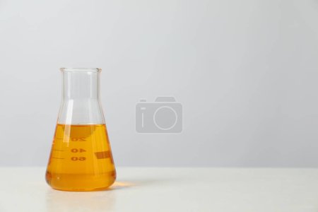 Photo for Glass flask with yellow oil on white table, space for text - Royalty Free Image
