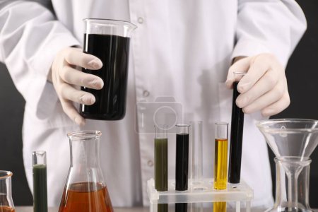 Photo for Woman holding beaker and test tube with black crude oil on dark background, closeup - Royalty Free Image