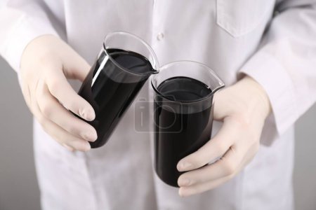 Photo for Woman pouring black crude oil into beaker on light background, closeup - Royalty Free Image
