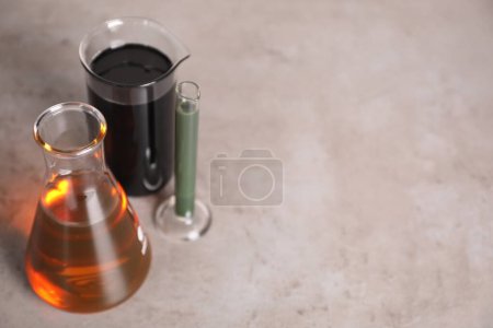 Test tube, beaker and flask with different types of oil on grey table, closeup. Space for text