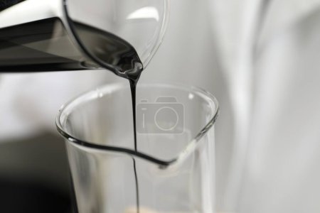 Pouring crude oil into beaker against blurred background, closeup