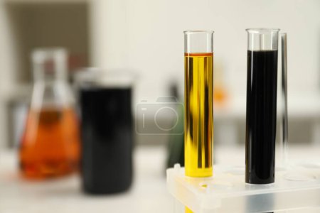 Test tubes with different types of crude oil against blurred background, closeup. Space for text