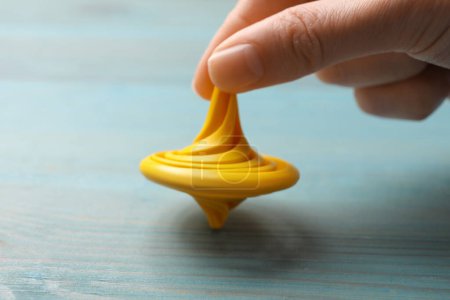 Woman playing with yellow spinning top at light blue wooden table, closeup