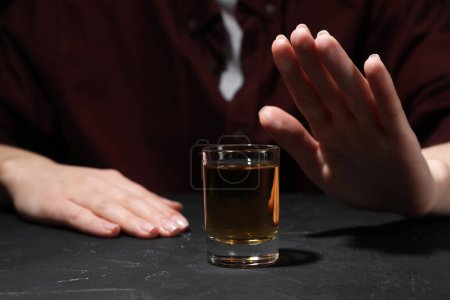Alkoholsucht. Frau verweigert Glas Whisky an dunkel strukturiertem Tisch, Nahaufnahme