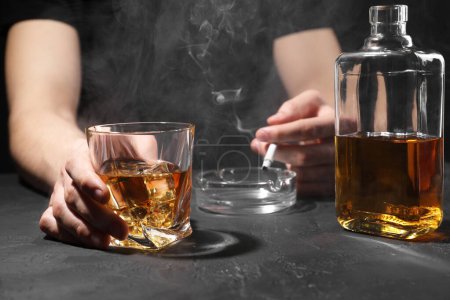 Adicción al alcohol. Hombre con whisky y cigarrillo humeante en la mesa de textura oscura, primer plano
