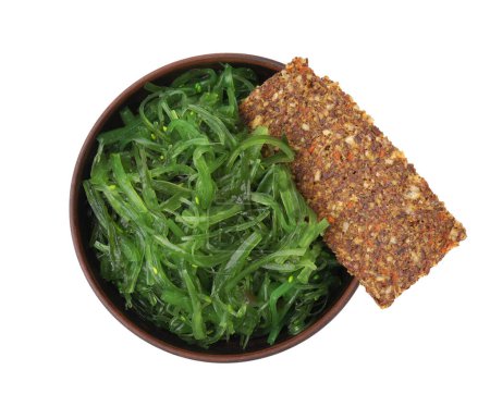 Tasty seaweed salad in bowl and crispbread isolated on white, top view