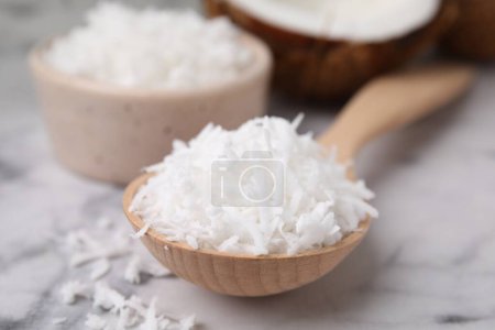 Photo for Coconut flakes in wooden spoon on white marble table, closeup - Royalty Free Image