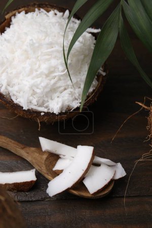 Photo for Coconut flakes, spoon, nut and palm leaf on wooden table - Royalty Free Image