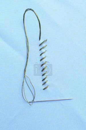 Sewing needle with thread and stitches on light blue cloth, top view