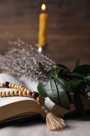Rosary beads, Bible and willow branches on table, closeup