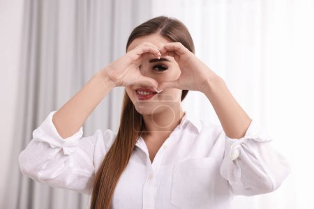 Glückliche Frau zeigt Herz-Geste mit Händen im Haus