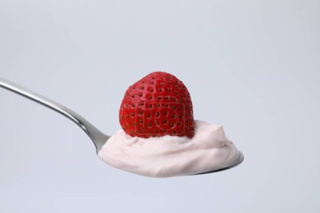 Delicioso yogur natural con fresa fresca en cuchara sobre fondo claro