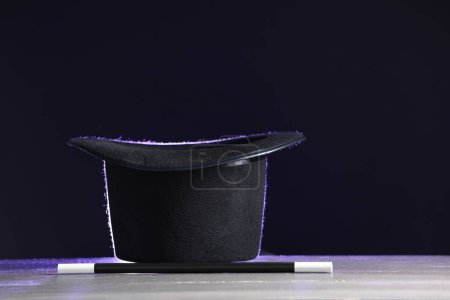 Sombrero de mago y varita sobre mesa de madera blanca sobre fondo negro