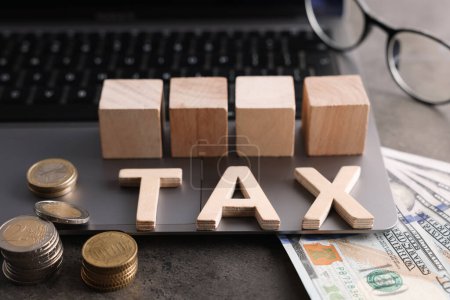 Word Tax made of wooden letters, cubes, laptop, banknotes and coins on grey table