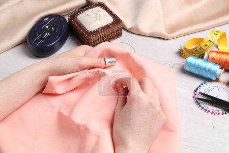 Woman with sewing needle and thread embroidering on cloth at white wooden table, closeup