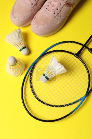 Photo for Feather badminton shuttlecocks, rackets and sneakers on yellow background, flat lay - Royalty Free Image