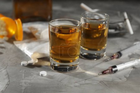 Photo for Alcohol and drug addiction. Whiskey in glasses, syringes, pills and cocaine on grey table, closeup - Royalty Free Image