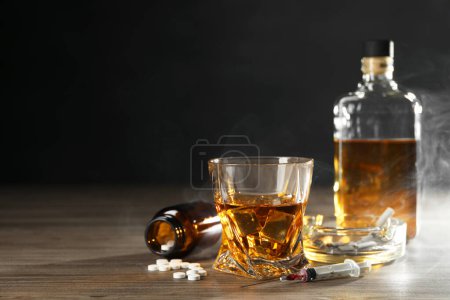 Photo for Alcohol and drug addiction. Whiskey in glass, syringe, pills and cigarettes on wooden table, space for text - Royalty Free Image