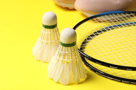 Photo for Feather badminton shuttlecocks, rackets and sneakers on yellow background, closeup - Royalty Free Image