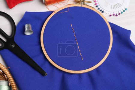 Téléchargez les photos : Tissu bleu avec points de suture, fil à coudre, aiguille et ciseaux sur table lumineuse, plat - en image libre de droit