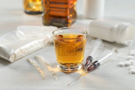 Photo for Alcohol and drug addiction. Whiskey in glass, syringes, cocaine and pills on white table - Royalty Free Image