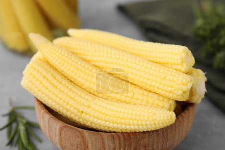 Tasty fresh yellow baby corns in bowl on grey table, closeup