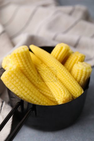 Tasty fresh yellow baby corns in dish on grey table, closeup