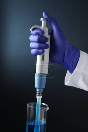 Photo for Laboratory analysis. Scientist dripping sample with micropipette into beaker on dark background, closeup - Royalty Free Image