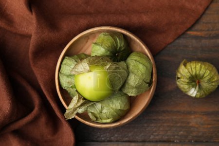 Fresh green tomatillos with husk in bowl on wooden table, top view