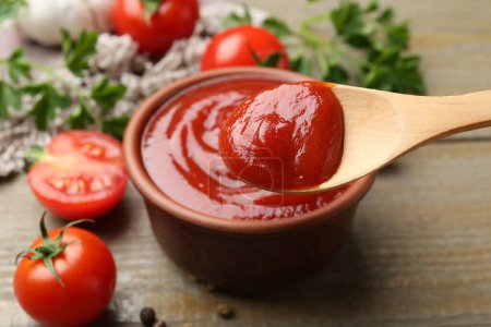 Photo for Bowl and spoon with tasty ketchup, fresh tomatoes, parsley and spices on wooden table - Royalty Free Image
