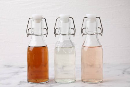 Different types of vinegar in bottles on light marble table, closeup