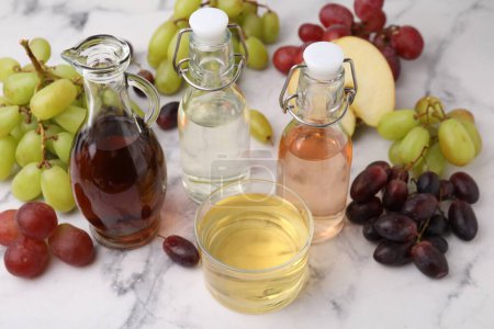 Different types of vinegar and grapes on light marble table, closeup